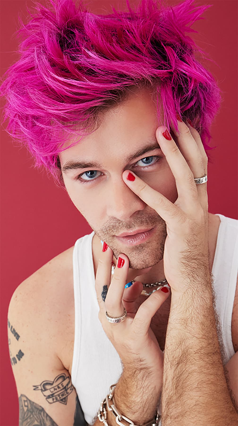 Stylish man with intense gaze, featuring Arctic Fox's Virgin Pink hair color, complementing his edgy look with painted nails and trendy jewelry.
