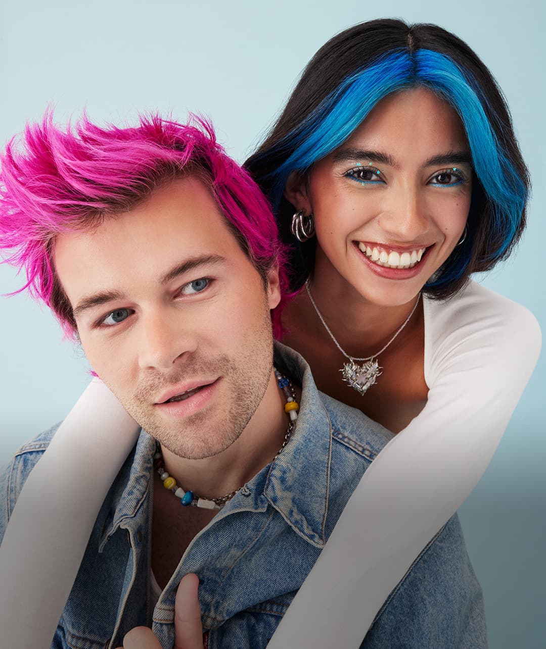 Portrait of a smiling couple showcasing Arctic Fox hair colors, with the man sporting vibrant Virgin Pink and the woman featuring bold Aquamarine highlights, both exuding style and confidence.